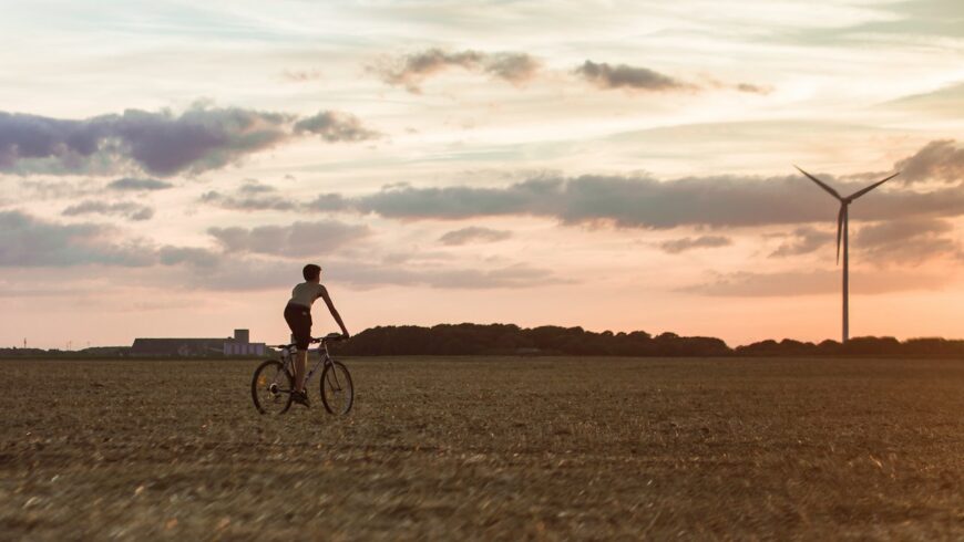 Una persona en una bicicleta en un campo por una turbina de viento